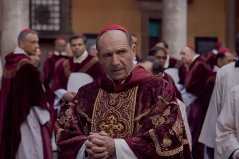 Scena z filmu o papieżu. Kardynał w bogato zdobionej szacie z czerwonym piuską. W tle inni duchowni.