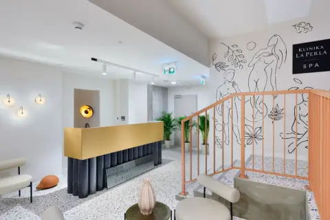 Nowoczesne wnętrze kliniki La Perla SPA w Nałęczowie. Złota recepcja, schody z brzoskwiniową balustradą i artystyczne rysunki na ścianie tworzą elegancką atmosferę.