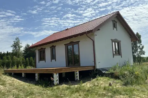 Nowy projekt domu drewnianego z tarasem, w otoczeniu zieleni.