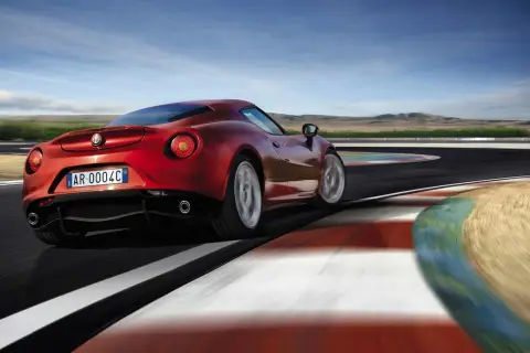 Czerwone Alfa Romeo 4C na torze wyścigowym, z rozmytymi kołami i kolorowymi bandami.