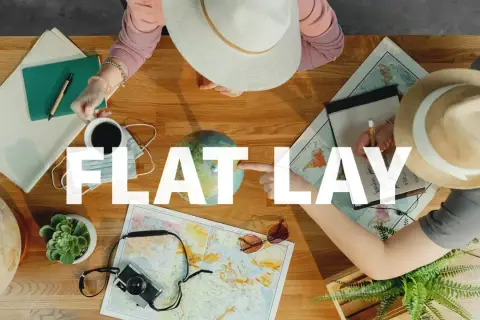Widok z góry na stół z mapami, globusem, aparatem, notatnikiem i kawą. Dwie osoby planują podróż, tworząc idealny **flat lay**.