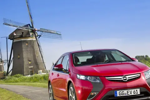 Czerwony Opel Ampera na tle wiatraków w Holandii.