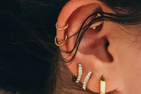 Ucho ozdobione złotymi kolczykami, w tym subtelnym conch piercingiem, podkreśla indywidualny styl.