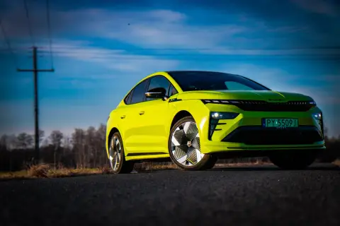 Jaskrawozielony Skoda Enyaq Coupe na tle błękitnego nieba z chmurami i linią energetyczną.