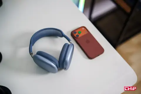 Niebieskie słuchawki AirPods Max i brązowy iPhone na białym biurku. Dowiedz się, jak połączyć AirPods z PC.