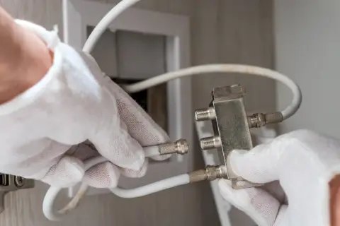 Ręce w białych rękawiczkach podłączają kabel antenowy do rozdzielacza.