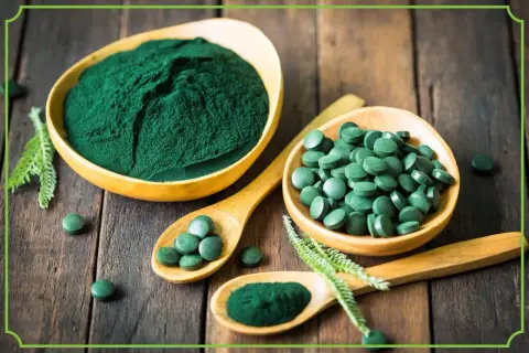 Zielona spirulina w proszku i tabletkach na drewnianym tle. Dowiedz się, spirulina co to jest i jakie ma właściwości.
