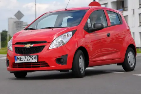 Czerwony Chevrolet Spark na drodze. Kierowca w środku. Wiele osób szuka chevrolet spark opinie przed zakupem.