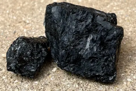 Dwa bryły czarnego kamienia szlachetnego, węgla, leżą na piasku.