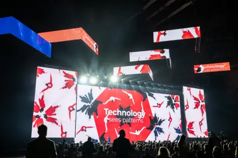 Wielkie ekrany na scenie pokazują ludzi w czerwonych strojach, tworzących wzory. To inspiracja, jak zarabiać na zdjęciach, wykorzystując kreatywność i technologię.