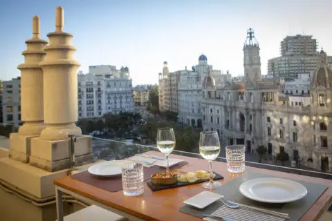 Una mesa en una terraza con vistas a la ciudad, con copas de vino y aperitivos, bajo el cielo de Atenea.