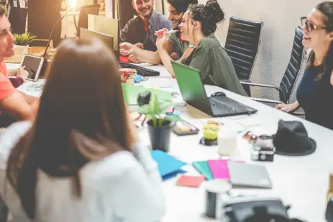 Uśmiechnięci millenialsi pracują razem przy biurku, otoczeni laptopami i tabletami.