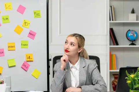 Młoda kobieta zastanawia się nad ścieżkami kariery po studiach marketing i zarządzanie, widząc na tablicy słowa kluczowe: plan, zespół, produkt, finanse, sprzedaż.