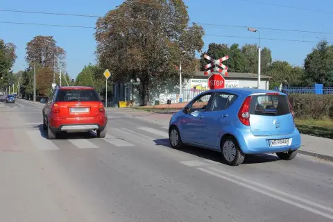 Czerwony i niebieski samochód na przejściu dla pieszych, czerwony czeka na wymijanie, niebieski już rusza.
