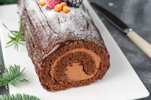 Bûche de Noël au chocolat, parfaite pour une recette génoise bûche moelleuse. Garnie de fruits rouges et de sucre glace.