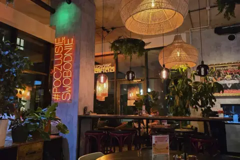 Wnętrze restauracji "Garnizon" z neonem "#POCZUJSIĘ SWOBODNIE", plecionymi lampami i roślinnością.