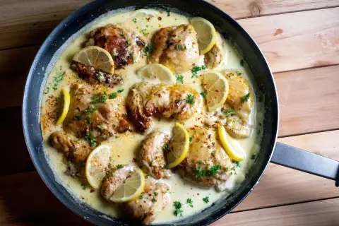 Succulento petto di pollo al limone in padella, guarnito con fette di limone fresco e prezzemolo tritato.
