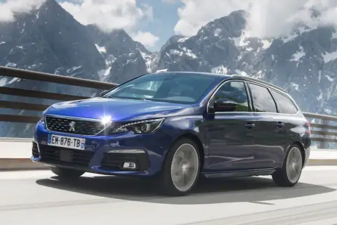 Niebieski Peugeot 308 T9 kombi jedzie po górskiej drodze, z ośnieżonymi szczytami w tle.