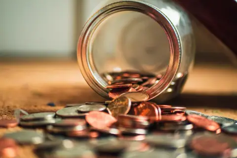 Słoik z monetami rozsypanymi na stole. Jak wyczyścić BIK po upadłości konsumenckiej? Czas na nowy początek finansowy.
