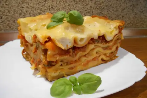 Pyszna, wielowarstwowa lasagne z sosem pomidorowym i serem, ozdobiona listkami bazylii. Idealna inspiracja, jak zrobić lasagne.