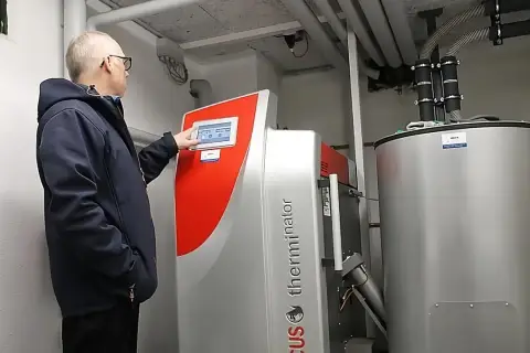 Mężczyzna obsługuje nowoczesny piec na pellet do salonu. Urządzenie z panelem dotykowym i dużym zasobnikiem zapewnia komfortowe ogrzewanie.