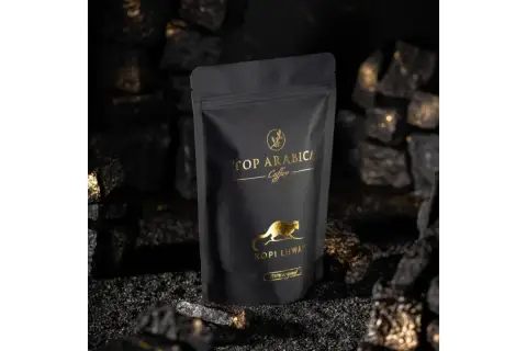 Czarna torebka z napisem "TOP ARABICA Coffee Kopi Luwak" i złotym rysunkiem zwierzęcia. To najdroższa kawa rozpuszczalna, otoczona węglem i złotymi drobinkami.