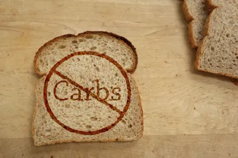 Kromka chleba z przekreślonym napisem "Carbs". Idealne dla osób szukających produktów bez węglowodanów, tabela z nimi może być pomocna.