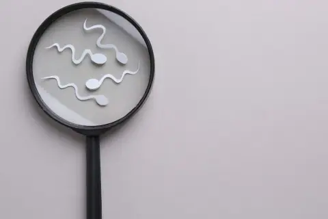 Spermy pod lupą. Wyglądają jak małe, białe kształty, które mogą symbolizować preejakulat lub plemniki.