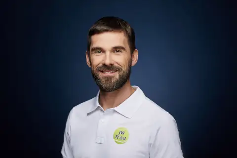 Paweł Habrat, uśmiechnięty mężczyzna z brodą, w białej koszulce polo z logo "JW TEAM".