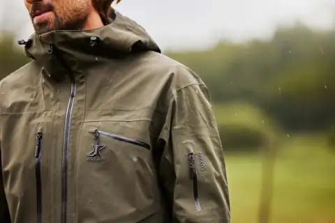 Mężczyzna w zielonej kurtce z kapturem, na której widać krople deszczu. Taka kurtka water repellent co to znaczy? To ochrona przed wilgocią.