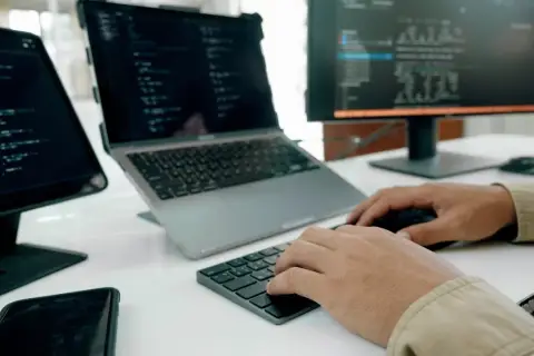 Programista pracuje nad nowym oprogramowaniem użytkowym, pisząc kod na laptopie i monitorze.
