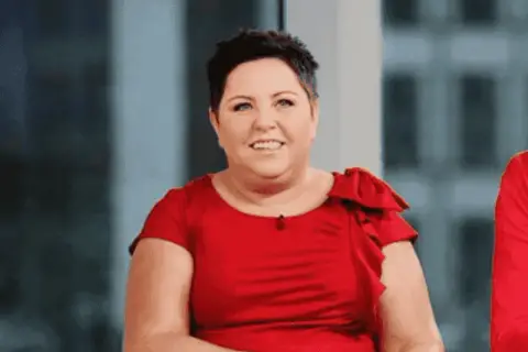 Uśmiechnięta Dorota Wellman w czerwonej sukience. Jej wiek nie jest widoczny, ale emanuje pewnością siebie.