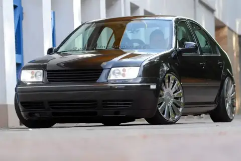 Czarny Volkswagen Bora z chromowanymi felgami stoi na ulicy.