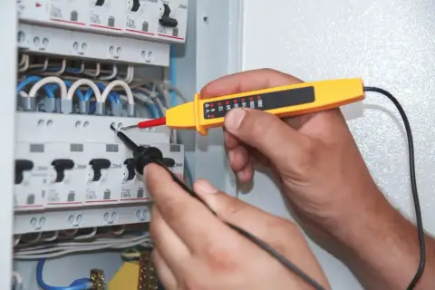 Elektryk sprawdza napięcie w skrzynce bezpieczników. Miernik wskazuje moc pozorną, pomagając zapewnić bezpieczeństwo instalacji.