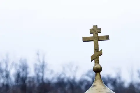 Złoty krzyż prawosławny na tle pochmurnego nieba. Symbolizuje nadzieję i pamięć podczas pogrzebu prawosławnego.