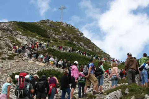 Tłum turystów podąża czerwonym szlakiem na Giewont. W oddali widoczny krzyż na szczycie.