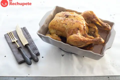Pollo asado dorado en una fuente, listo para servir. Ideal para tus recetas con pollo. Cubiertos y servilleta a un lado.
