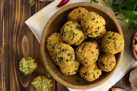 Schüssel mit frittierten Falafel-Bällchen, die aus frischen falafel zutaten zubereitet wurden. Daneben liegen Knoblauch und Kräuter.