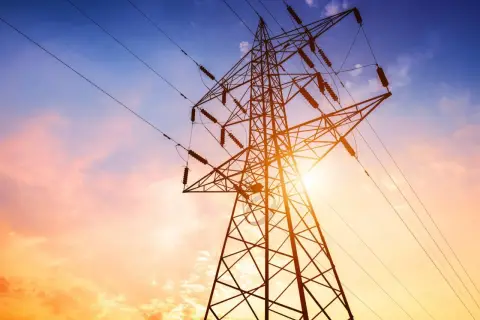 Słupy energetyczne na tle zachodzącego słońca. Zastanawiasz się, ile wynosi odszkodowanie za słupy energetyczne na działce?