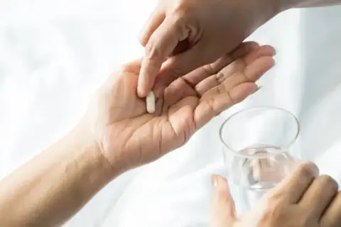 Dłoń podaje kapsułkę, symbolizującą wsparcie dla mózgu po antydepresantach. Obok szklanka wody.