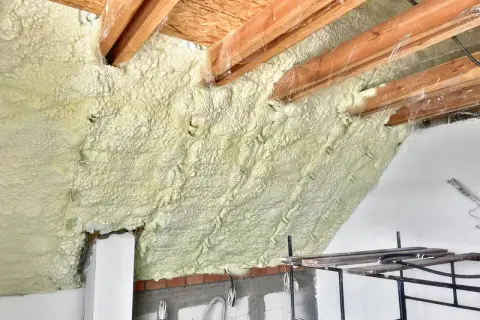Ocieplanie pianką poddasza. Widoczne drewniane krokwie i warstwa izolacji. Sprawdź ocieplanie pianką cena za m2.