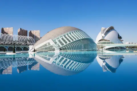 El Hemisfèric de Valencia, con su reflejo en el agua, se alza majestuoso bajo un cielo azul.