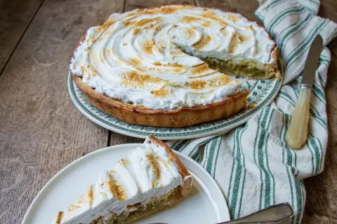 Tarte à la rhubarbe sur pâte feuilletée, recouverte d'une meringue dorée. Une part est servie sur une assiette.