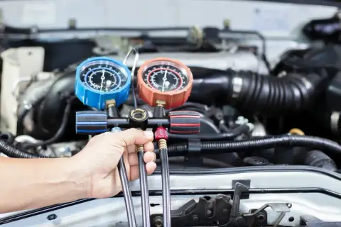 Mechanik sprawdza ciśnienie czynnika r1234yf w układzie klimatyzacji samochodu za pomocą manometrów.