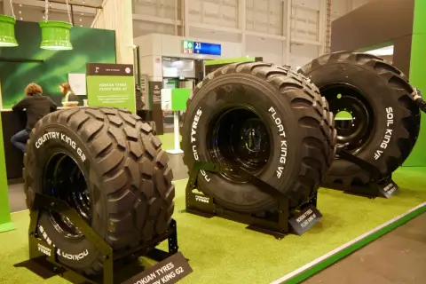 Trzy duże opony rolnicze Nokian Tyres na zielonej wykładzinie.