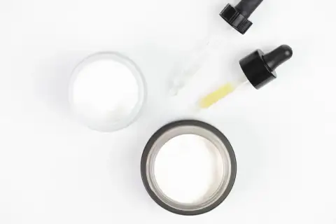 Dwa słoiczki z kremem i pipetki z serum, w tym z kwasem glikolowym, na białym tle.
