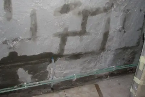 Ściana z widocznymi zaciekami i wilgocią, świadczącymi o jej higroskopijności. Widać instalację wodną.