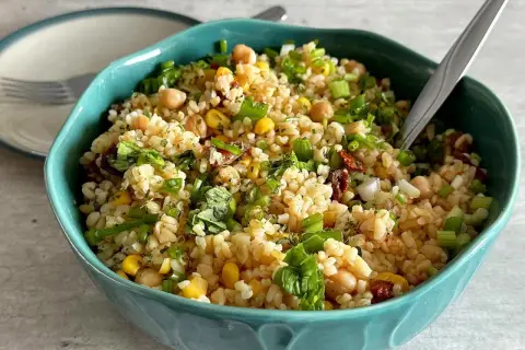 Kolorowa sałatka z kaszą bulgur, ciecierzycą, kukurydzą i suszonymi pomidorami, posypana szczypiorkiem.