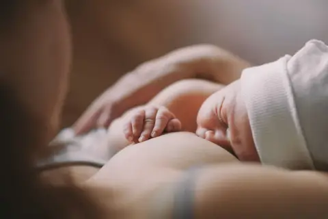 Delikatne dłonie noworodka obejmujące pierś podczas karmienia. Ulewanie u noworodka to częsty widok, ale ten moment to czysta bliskość.