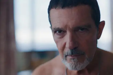 Zbliżenie na twarz Antonio Banderasa, z siwiejącą brodą i zmarszczkami. Jego spojrzenie jest intensywne.